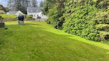 A grassy yard with a barbecue grill, a wooden fence, and a house in the background.