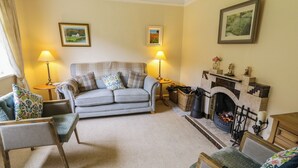 A cozy living room with a grey sofa, two armchairs, a fireplace, and two lamps. - James Neills Cottage (Maghernalaght)