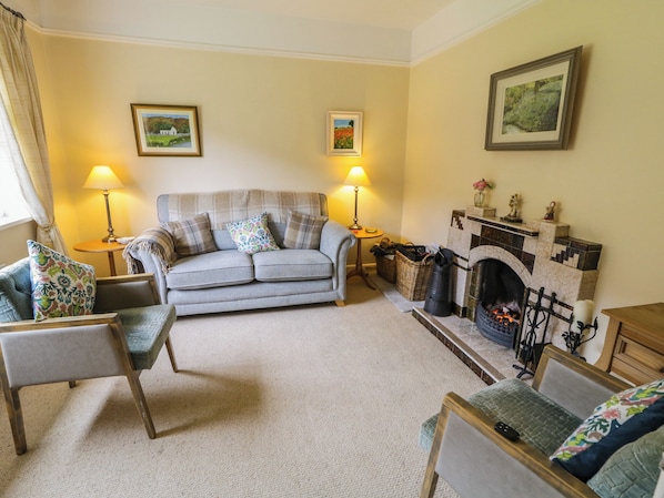 A cozy living room with a sofa, armchairs, a fireplace, and two lamps. - James Neills Cottage (Maghernalaght)