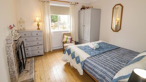 A bedroom with a bed, a dresser, a chair, a wardrobe, a window with curtains, and a mirror on the wall. - James Neills Cottage (Maghernalaght)