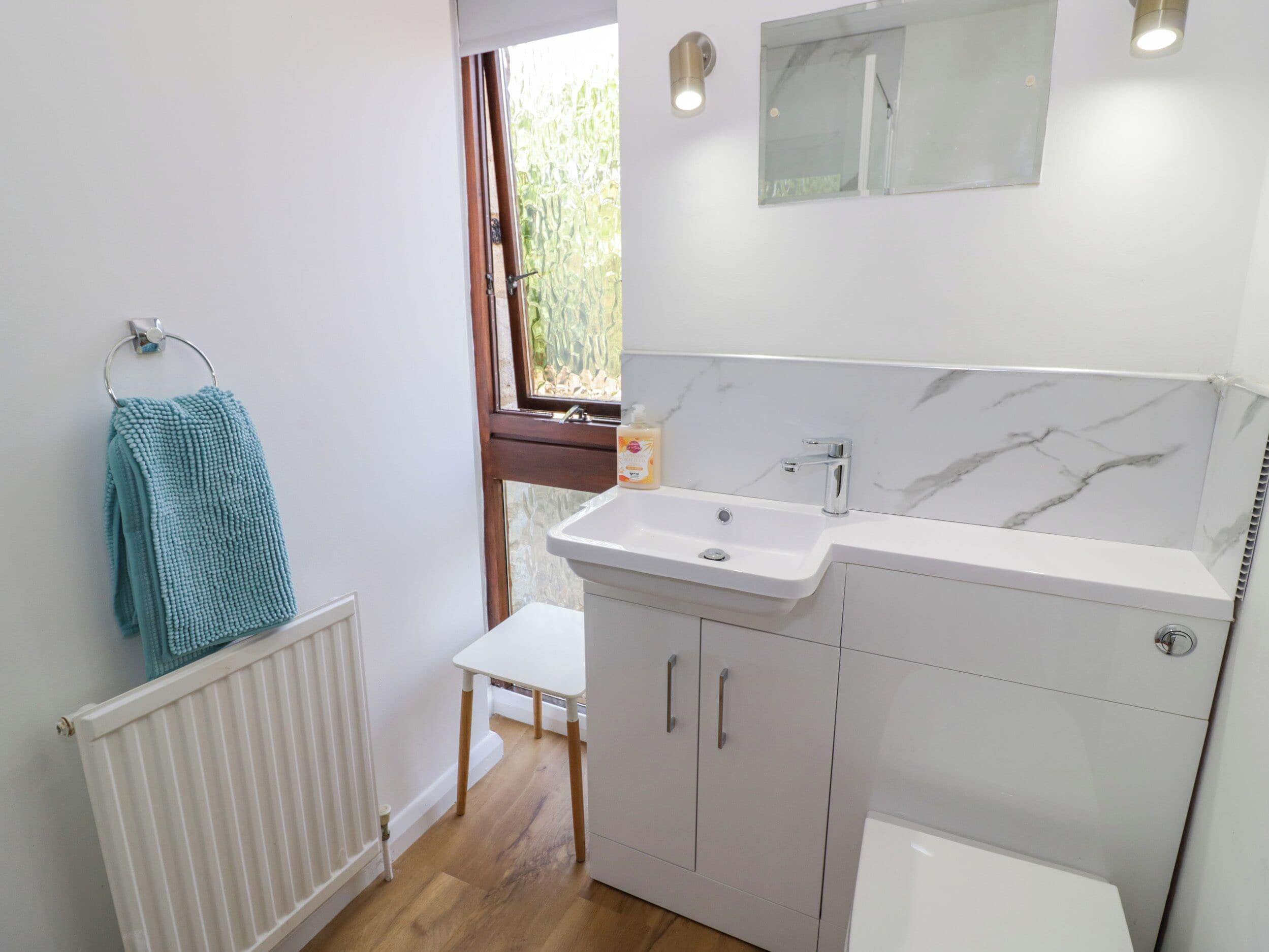 Une salle de bain avec un lavabo blanc, un pare-feu en marbre et une fenêtre donnant sur un paysage verdoyant.