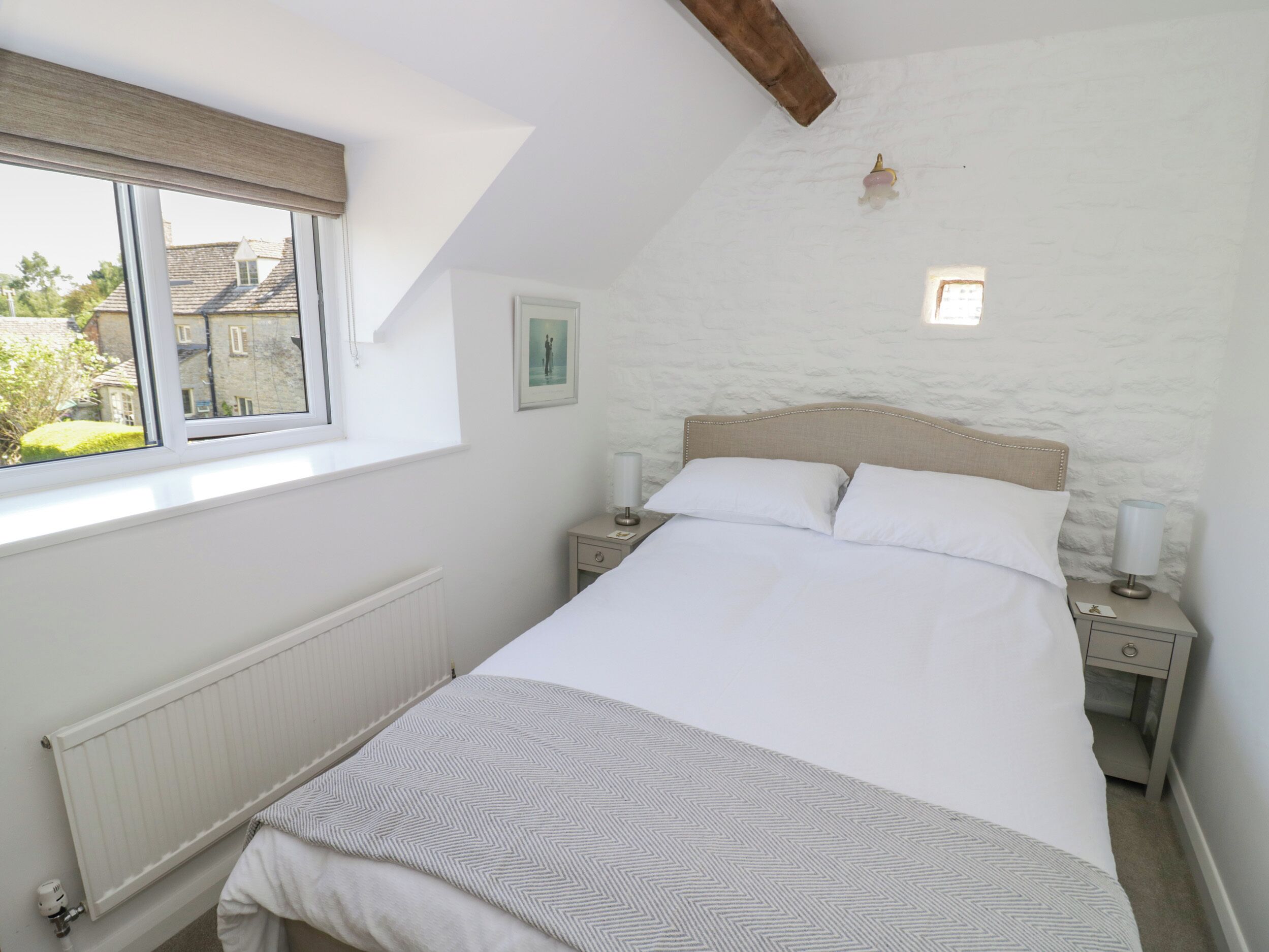 Un dormitorio con cama, mesitas de noche, ventana y radiador.