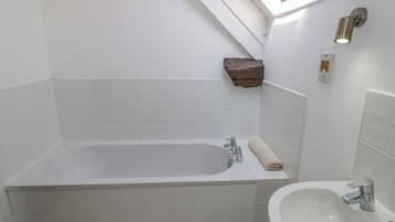 A modern bathroom with a freestanding bathtub, a sink, and a skylight above.