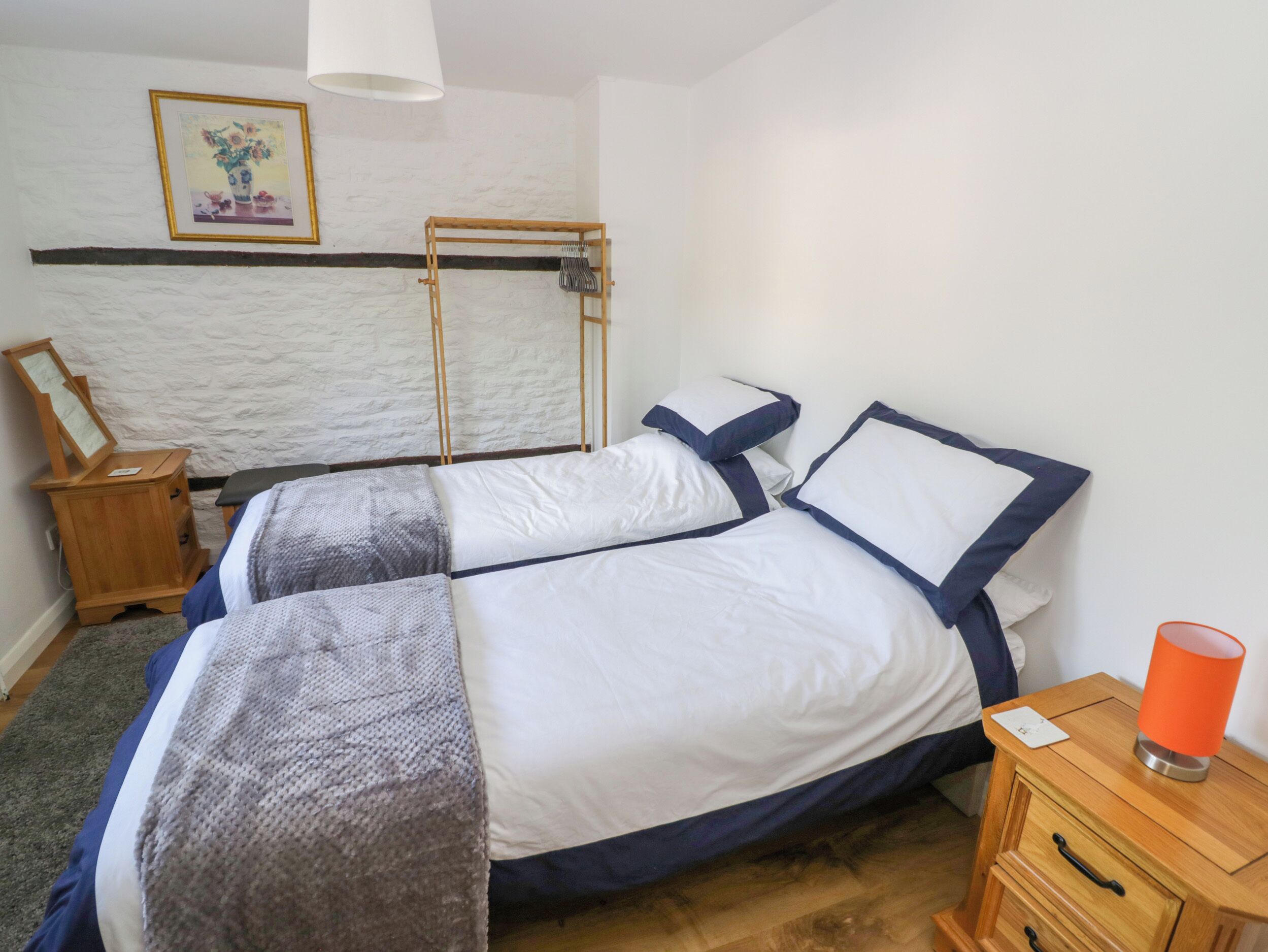 A bedroom with two beds, a wooden nightstand, a lamp, and a framed picture on the wall.