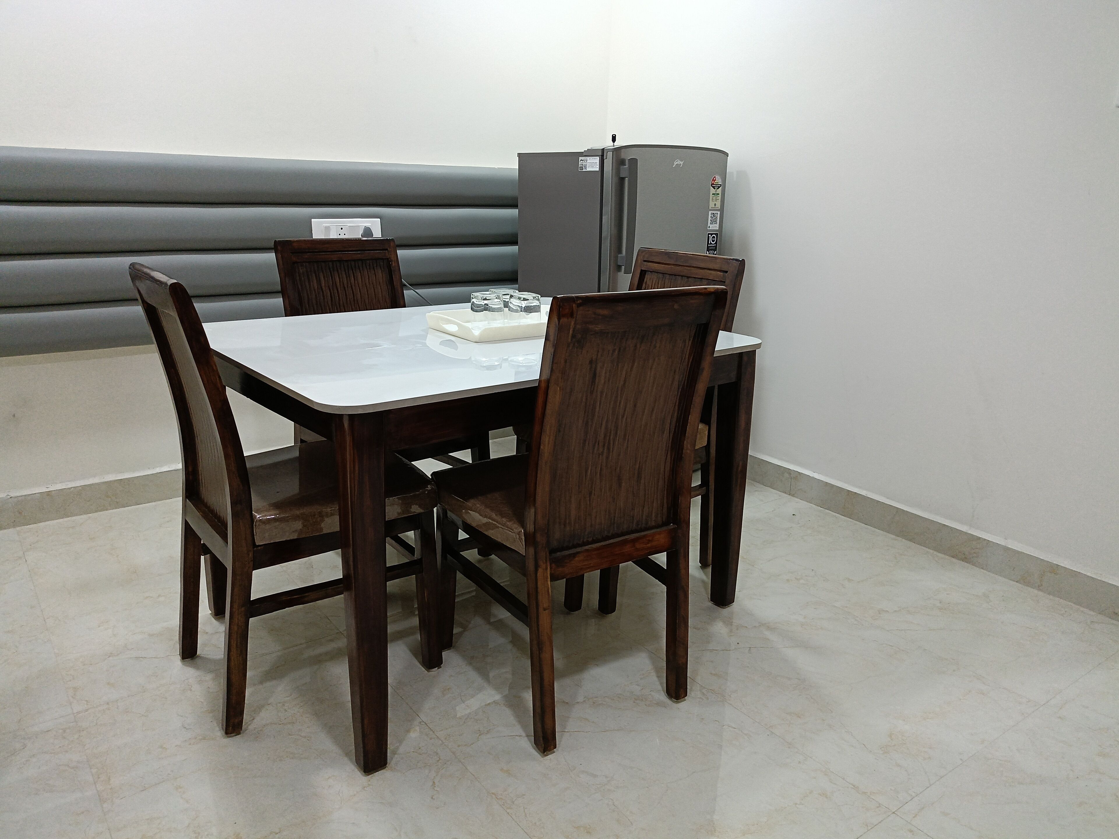 A dining table with four chairs, a small white table runner, and a refrigerator in the background.