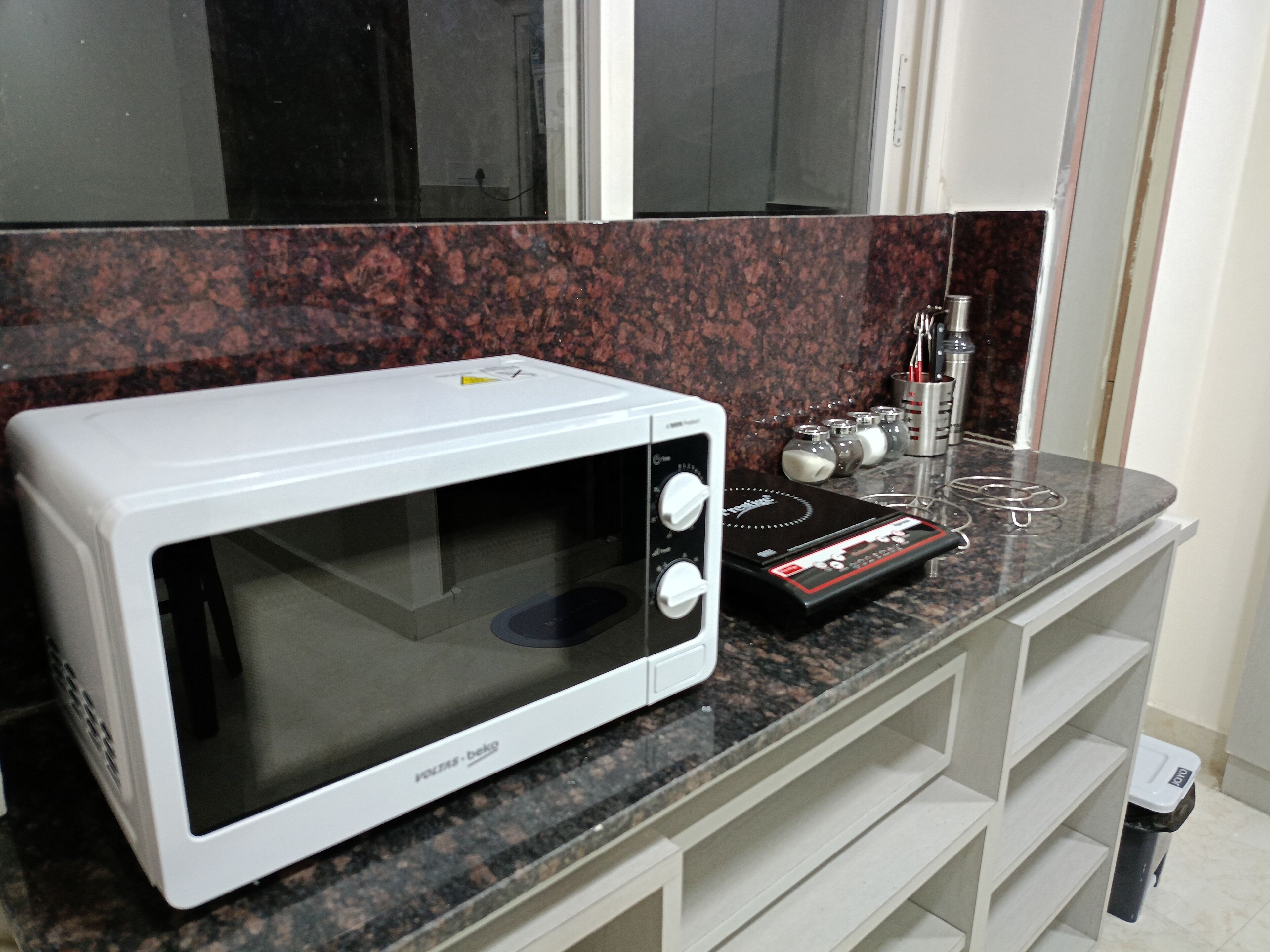 Un horno microondas blanco sobre una encimera de granito en una cocina con ventana.