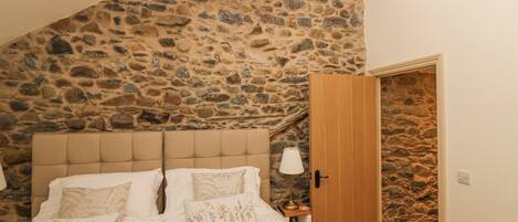 Une chambre avec un mur en pierre, une porte en bois et un lit agrémenté d’oreillers à motifs floraux.