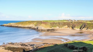Un paysage côtier avec une plage de sable, des collines verdoyantes et un ciel bleu dégagé.