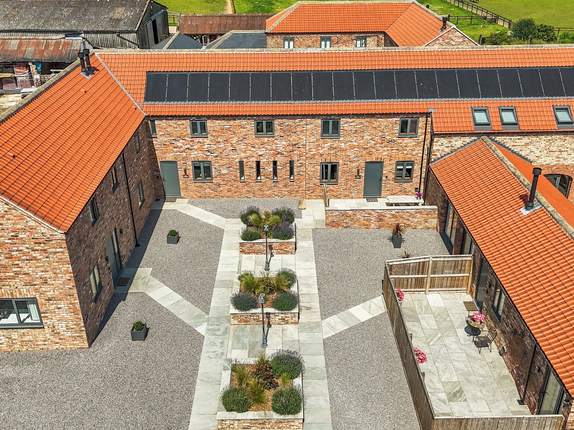 A courtyard with a central pathway, surrounded by buildings with brick facades and orange-tiled roofs.