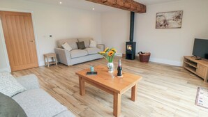 A living room with a sofa, a wooden coffee table, a fireplace, and a television. - The Hay Barn (Thirsk)