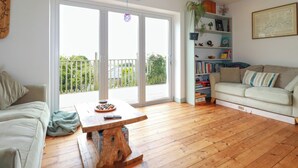 Ein geräumiges Wohnzimmer mit einem Holztisch, einem beigefarbenen Sofa und einem Bücherregal voller Bücher und Dekoration.