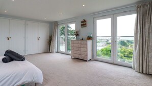 Ein Schlafzimmer mit großem Fenster, einem Bett, einem Schminktisch und einem Kleiderschrank.