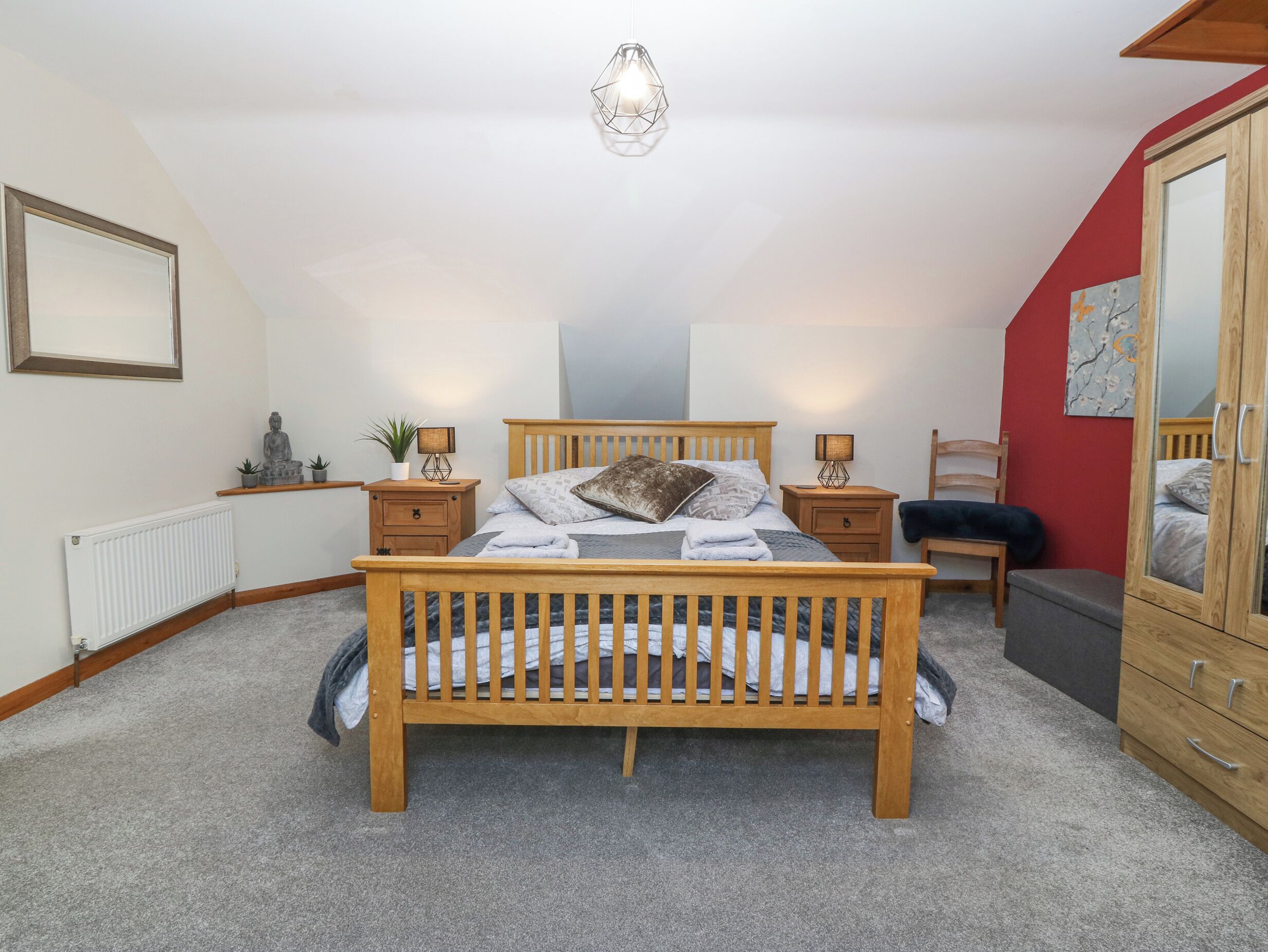 A bedroom with a wooden bed, bedside tables, a radiator, a mirror, and a ceiling light fixture.