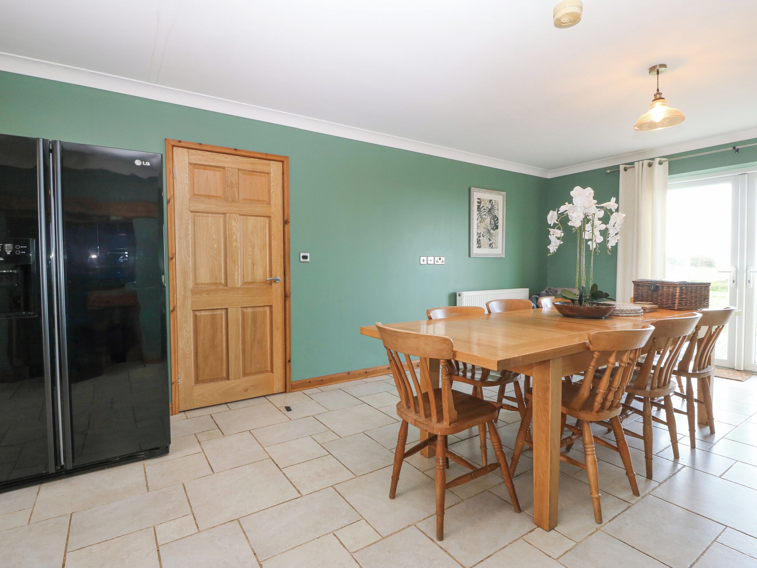 Un comedor con una mesa y sillas de madera, un refrigerador negro y una puerta de madera.