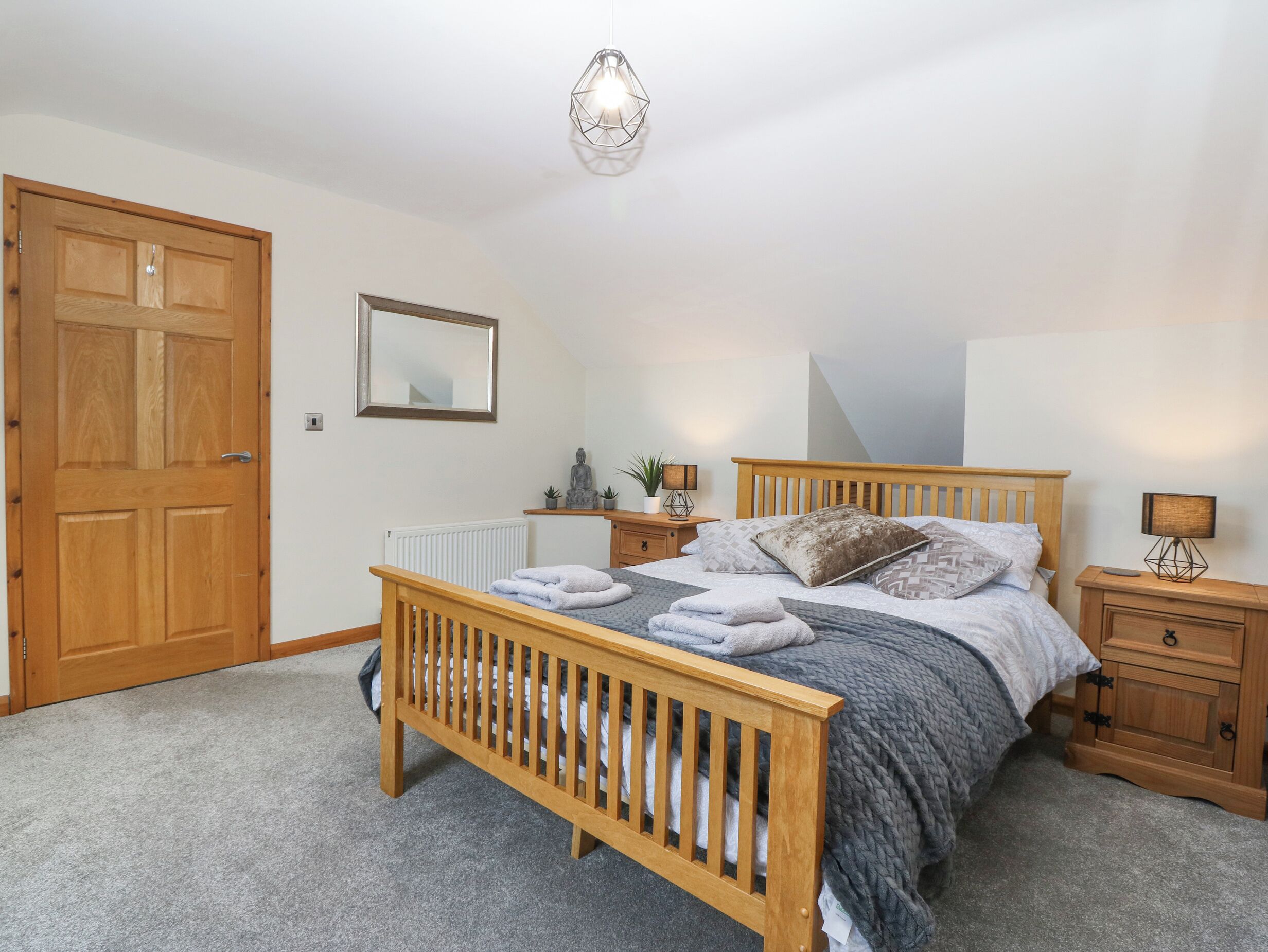 Une chambre à coucher avec un lit en bois, une table de chevet, une commode, un radiateur, un miroir et une porte.