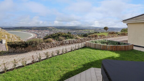 A view of a coastal town from a backyard with a stone wall, a grassy lawn, and a wooden deck.