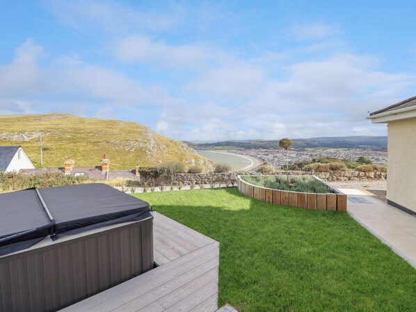 A backyard with a hot tub, a grassy lawn, and a view of a coastal town.