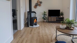 A living room with a wood-burning stove, a TV, and a dining area with a table and chairs.
