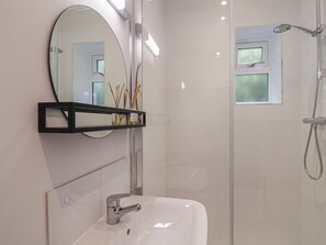 A bathroom with a white sink, a mirror, and a shower. - The Bungalow (Lyme Regis)