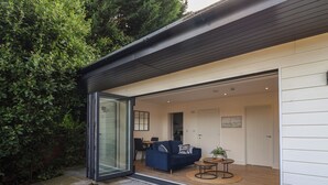A modern house with a glass door leading to a living area with a blue sofa, a small round table, and a potted plant.