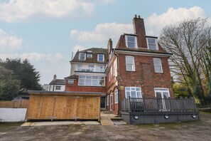 A two-story brick house with a wooden garage door, a fenced yard, and a staircase leading to the front door. - The Bungalow (Lyme Regis)