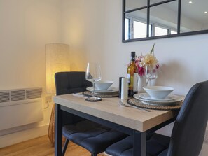 A dining area with a table set for two, featuring a lamp, wine bottles, and a vase with flowers. - The Bungalow (Lyme Regis)
