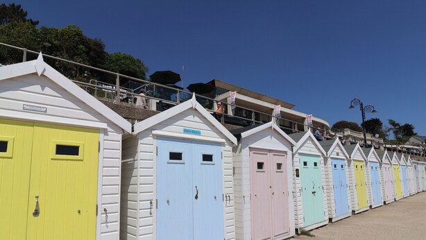 A row of colorful beach huts with white exteriors and pastel-colored doors.