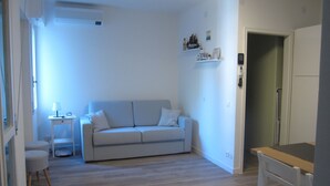 A living room with a light-colored sofa, a small table with a lamp, and a chair. - Retreat in Grado Just 100m From the Beach (Grado)