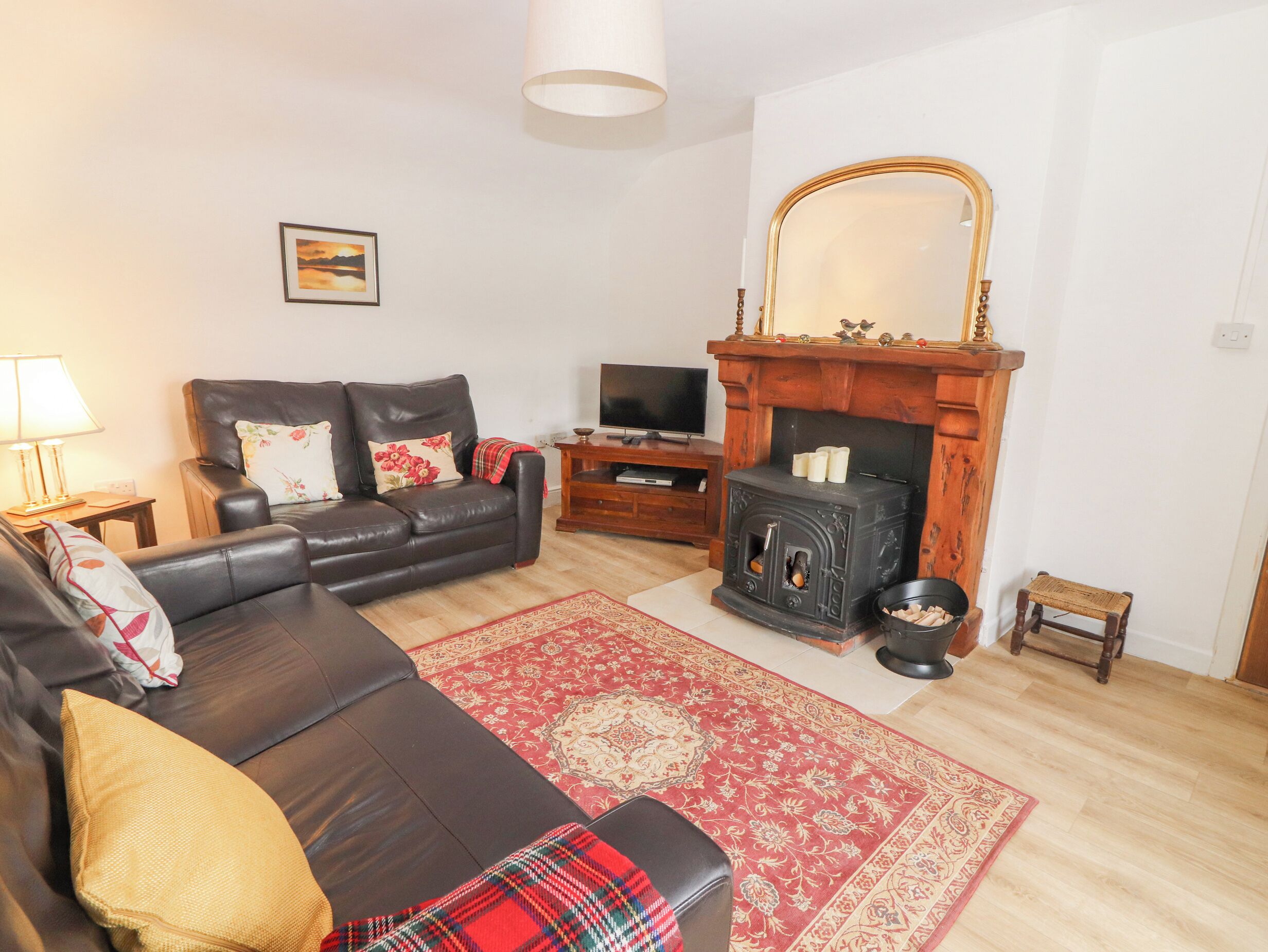 A living room with a leather sofa, a red patterned rug, a fireplace, a television, and a small wooden stool.