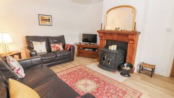 A living room with a leather sofa, a red patterned rug, a fireplace, a television, and a small wooden stool.