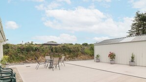 Une terrasse extérieure avec une table et des chaises, entourée de plantes en pot et avec un bâtiment en arrière-plan.