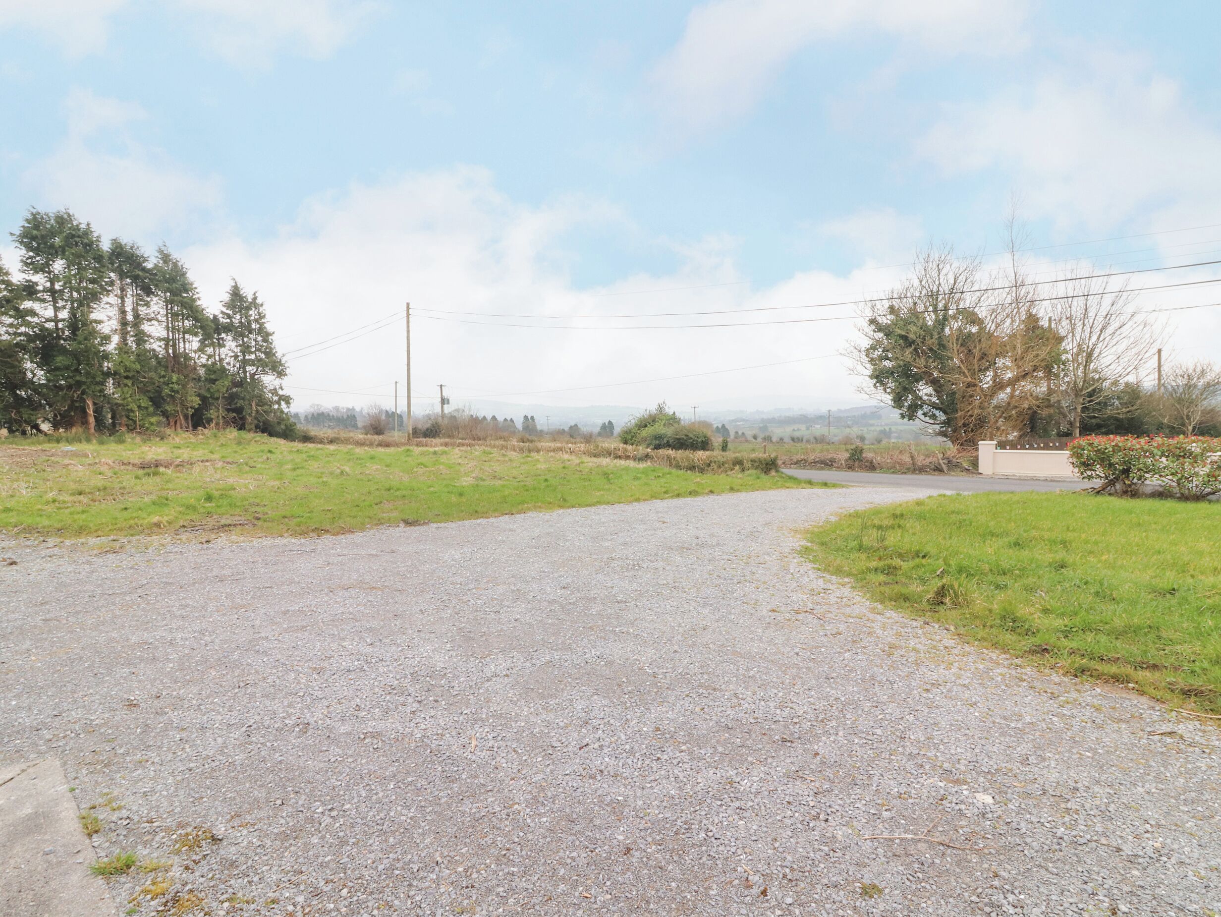 A gravel road curving to the right, surrounded by grassy fields and trees.