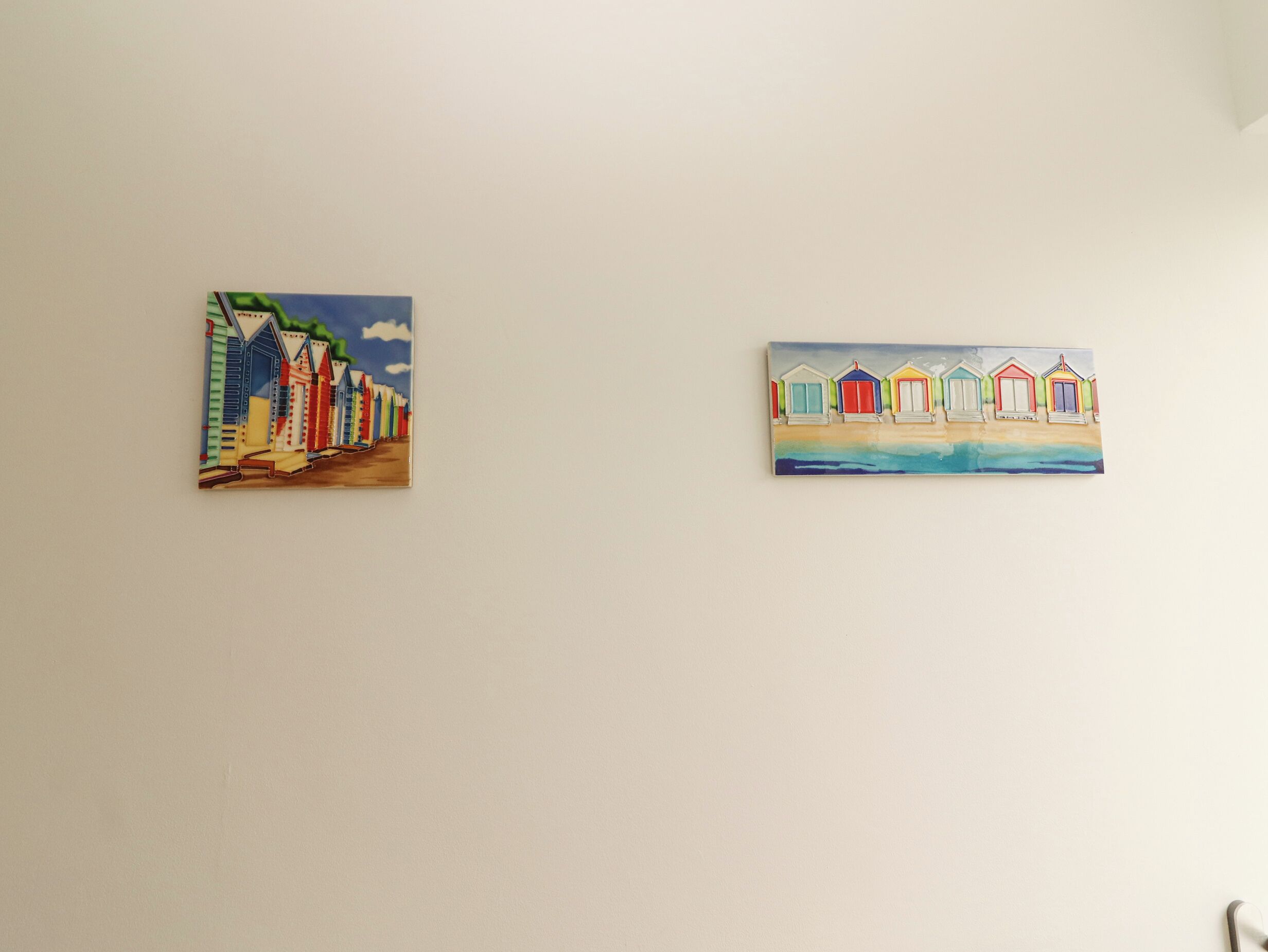Due dipinti raffiguranti casette sulla spiaggia colorate su un muro neutro.