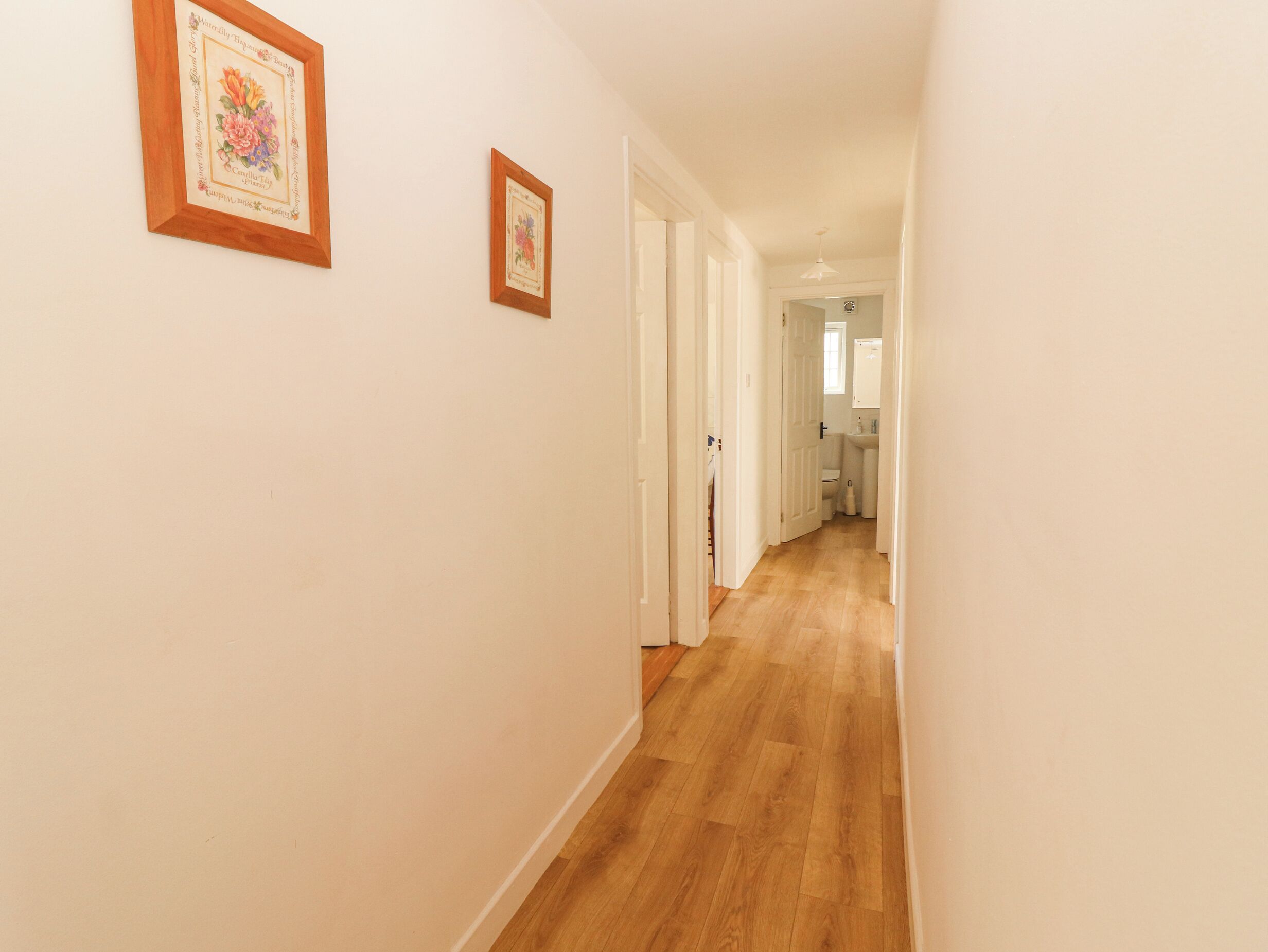 A hallway with wooden flooring and white walls, leading to a bathroom with a sink and toilet.