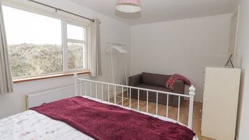 Un dormitorio con cama, ventana, radiador, armario blanco y lámpara colgante.