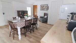 Un coin repas avec une table en bois dressée pour six personnes, entourée de chaises. Il y a également un coin cuisine équipé d’un réfrigérateur et d’un four à micro-ondes.