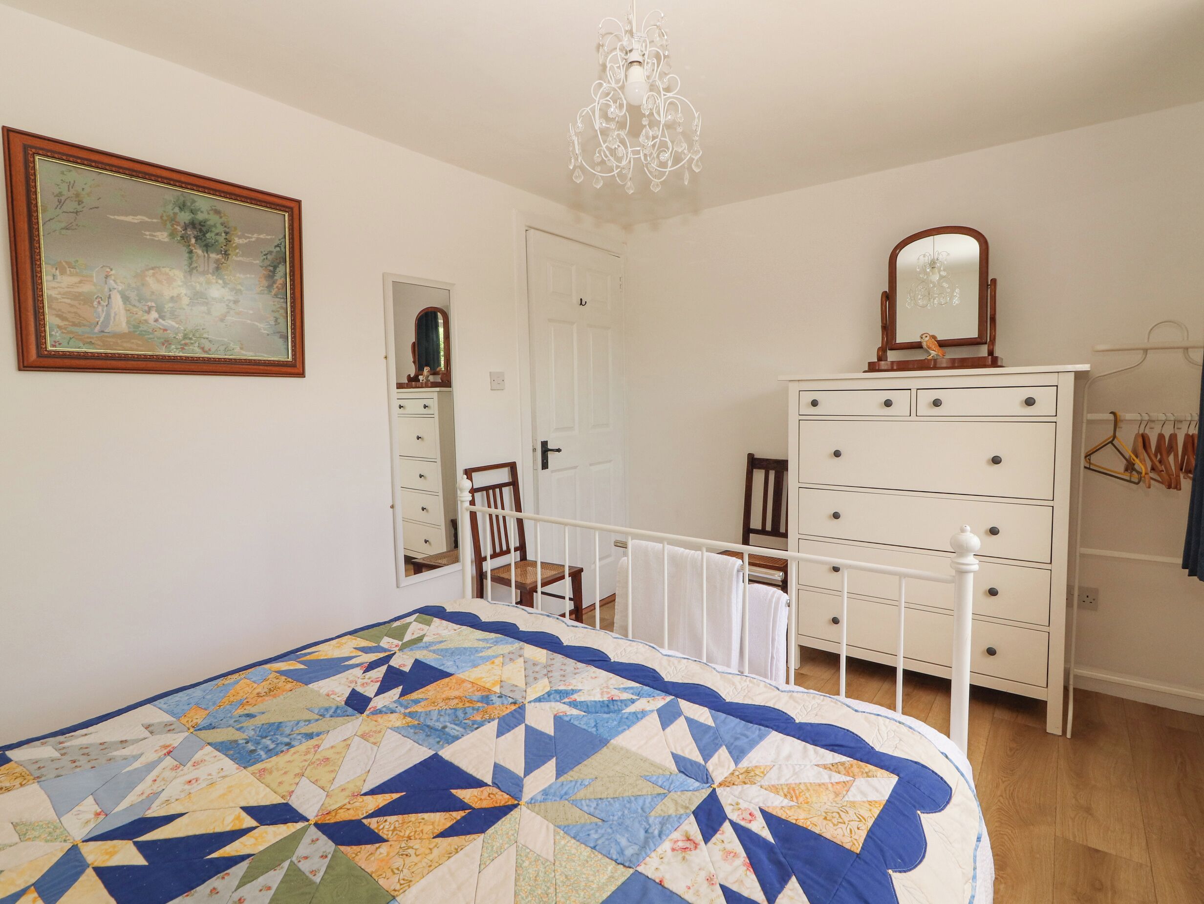 A bedroom with a bed, dresser, mirror, and a painting on the wall.