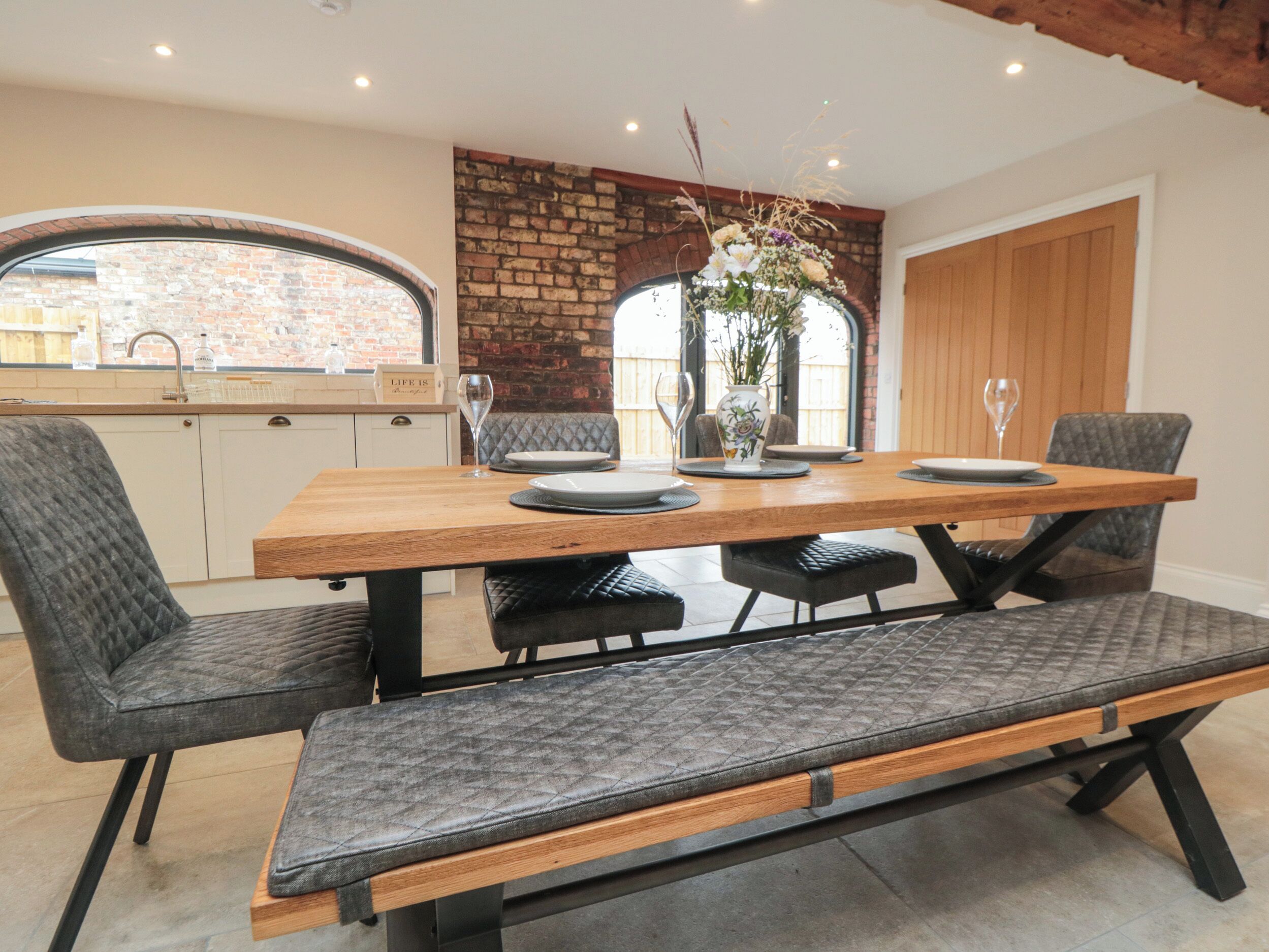 Een eetgedeelte met een houten tafel, grijs gestoffeerde stoelen en een bank.