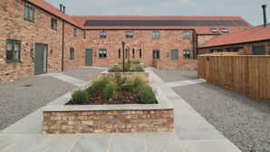 Une cour avec un bâtiment en briques, une clôture en bois et un espace jardin aménagé.