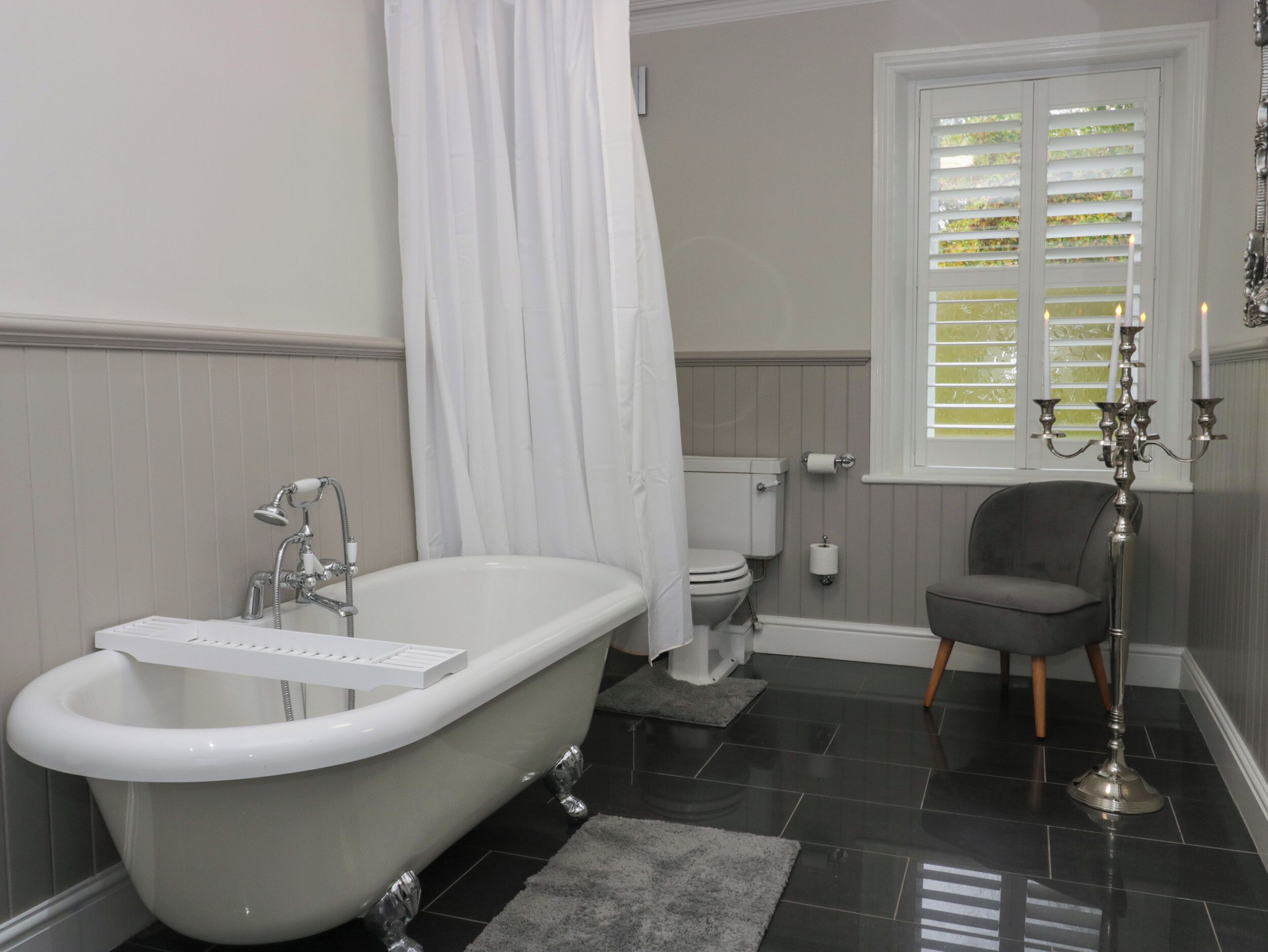 Une salle de bain avec une baignoire sur pieds, des toilettes, une douche et une fenêtre avec des volets.