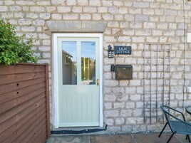 A stone cottage with a wooden door and a sign reading "LILAC COTTAGE".