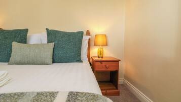 A neatly made bed with green and white pillows, a bedside lamp, and a wooden nightstand.