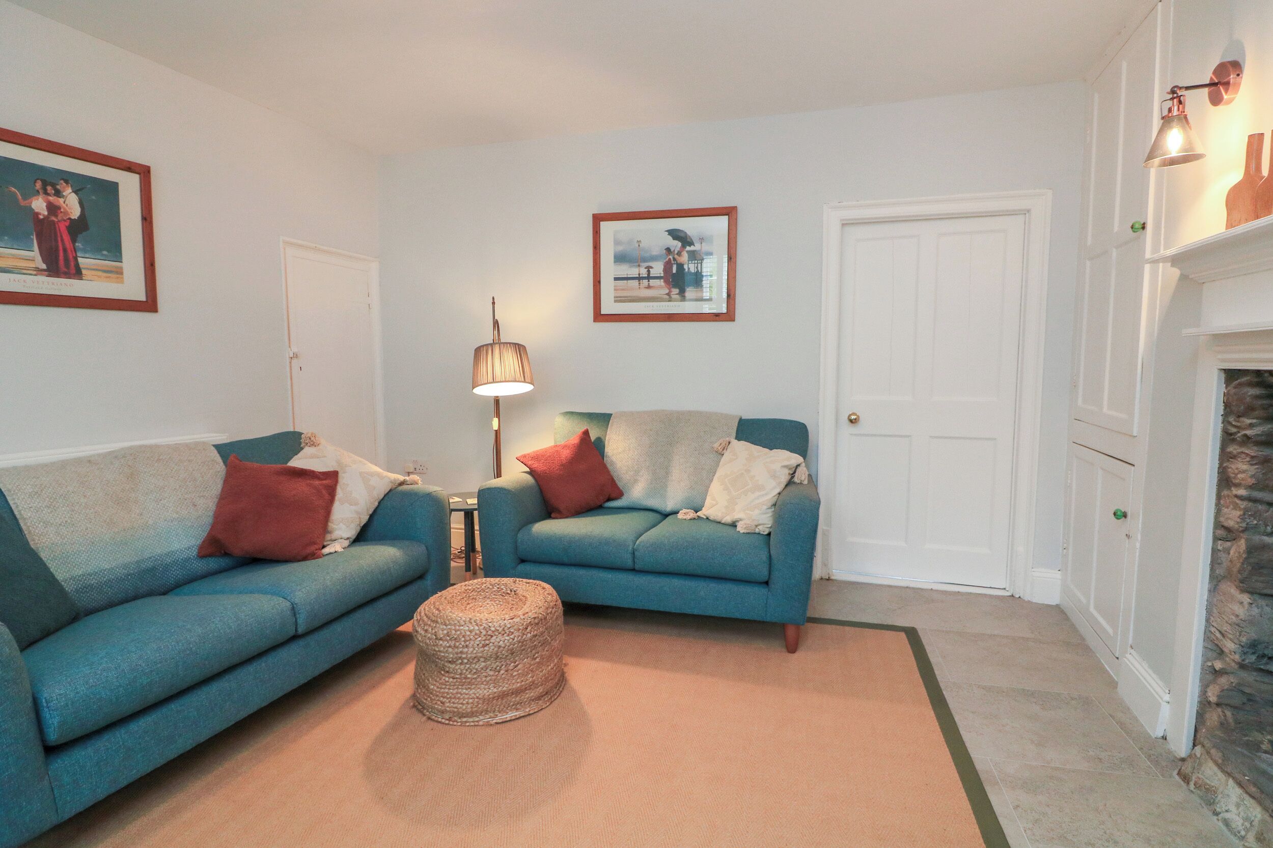 A living room with two blue sofas, a woven ottoman, a lamp, and a fireplace.