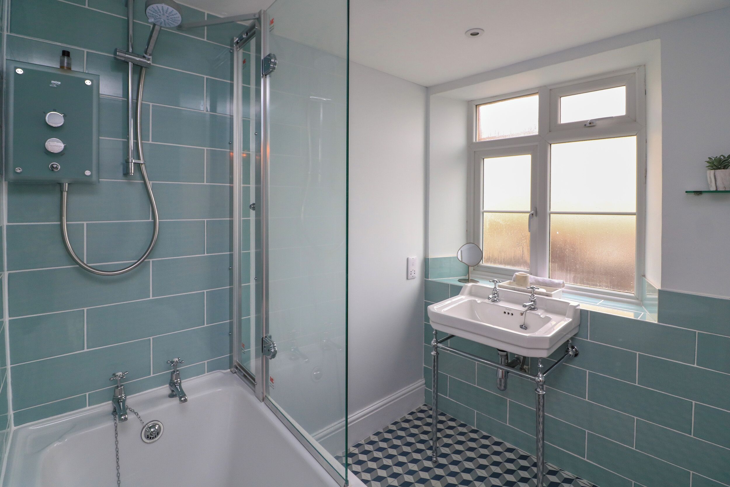 Une salle de bain avec une douche à parois de verre, une baignoire blanche et un lavabo placé sous une fenêtre.