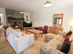 A cozy living room with a stone fireplace, a television, and comfortable seating. - Ysgubor Wen (Trefriw)