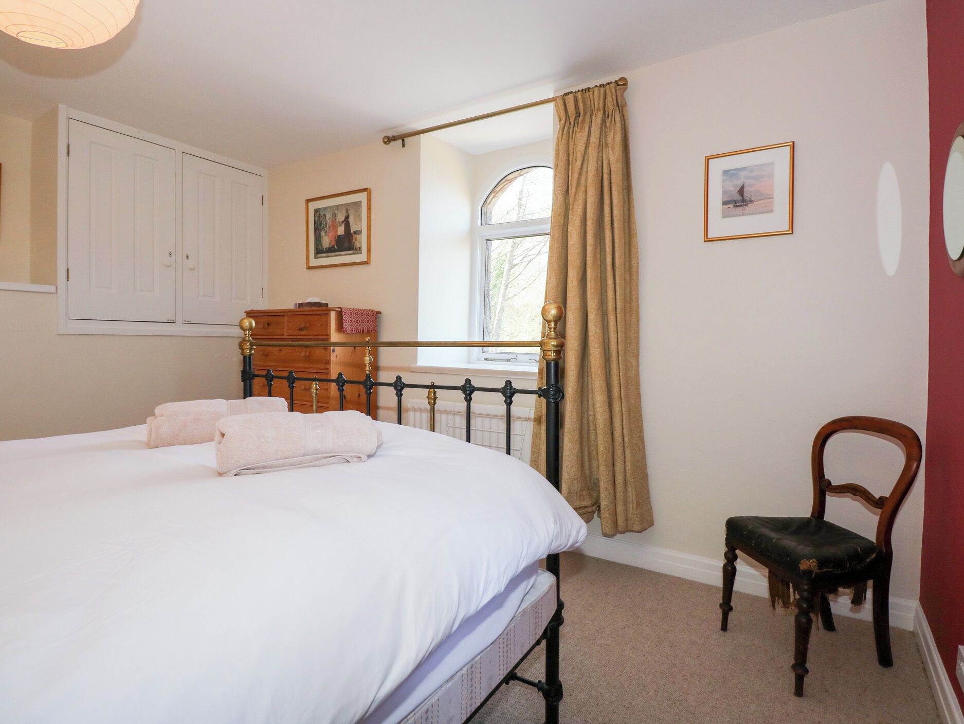 A bedroom with a bed, a wooden dresser, a chair, and a window with curtains.