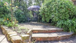 A garden with a stone bench, a small fountain, and lush greenery.