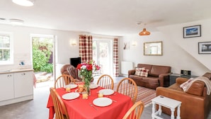 A dining area with a red tablecloth, wooden chairs, and a vase of flowers. There is a brown sofa and a white table in the living area.