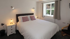 A bedroom with a large bed, bedside lamps, a window with curtains, and a radiator.