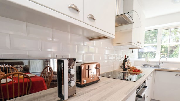 A modern kitchen with white cabinets, a wooden countertop, a toaster, and a dining area with a red tablecloth.